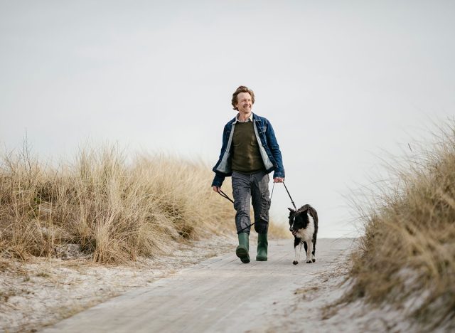 Middle aged caucasian man walking his border collie dog on a winter beach