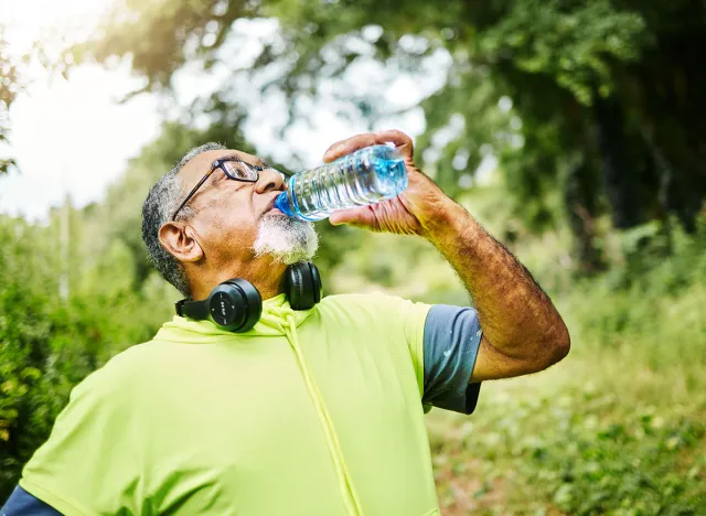 Senior man, fitness and drinking water in nature for hydration or natural sustainability after workout. Mature male person with mineral drink from exercise, training or cardio in recovery or break