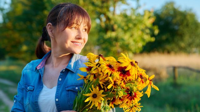 Profile view, happy middle aged woman with flowers looking at setting sun