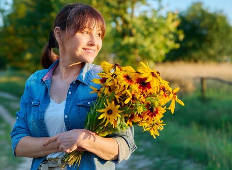 Profile view, happy middle aged woman with flowers looking at setting sun