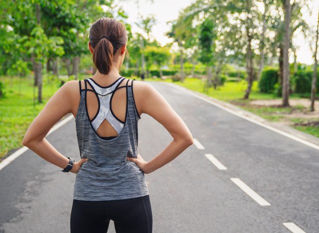 Back view of young fitness woman running on the road in the morning. People and sport concept, Sun light flare, Selective focus