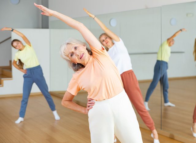 Positive mature woman doing aerobics exercises with group of people in dance center