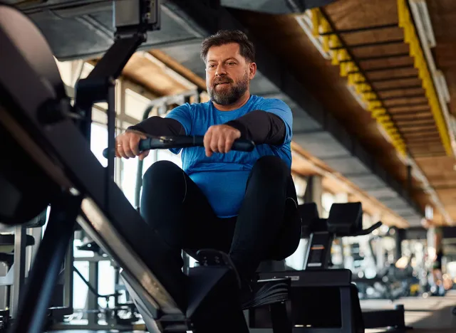 Mature athlete using rowing machine while working out in a gym.