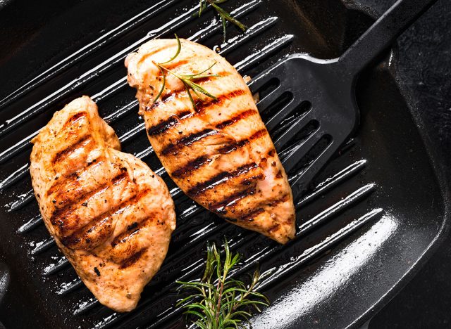 Grilled Chicken Breast Fillet on grill pan with rosemary close up. Grilled meat steak on rustic black background.