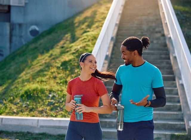 Happy multiracial athletic couple talking while having sports training outdoors. Copy space.