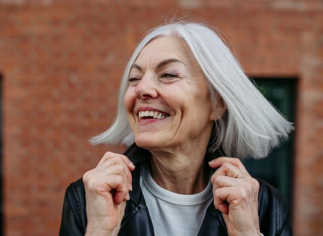 Portrait of stylish mature woman with gray hair on city street. Older woman in leather jacket smiling.