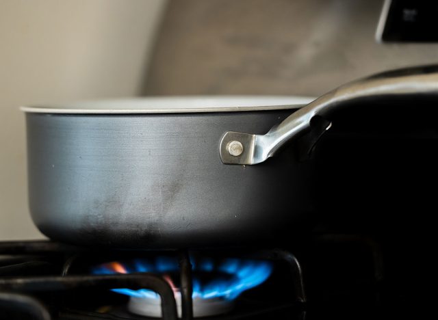 Close-up of a frying pan on a gas stove burner with blue flames