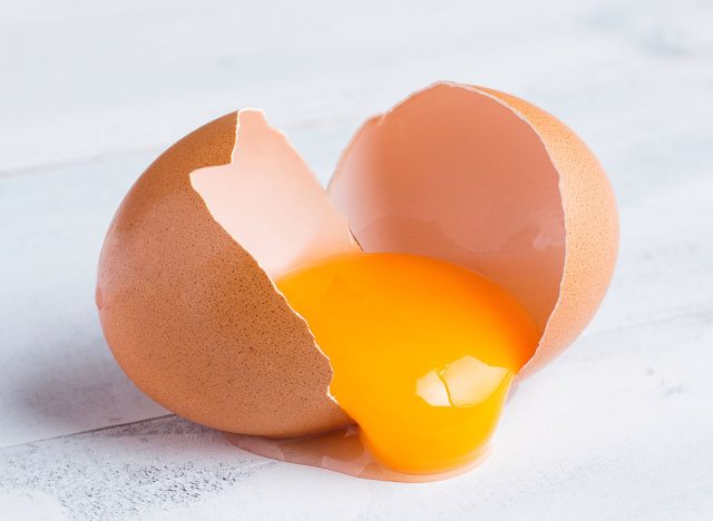 raw broken chicken egg , egg yolk in shell on white wooden