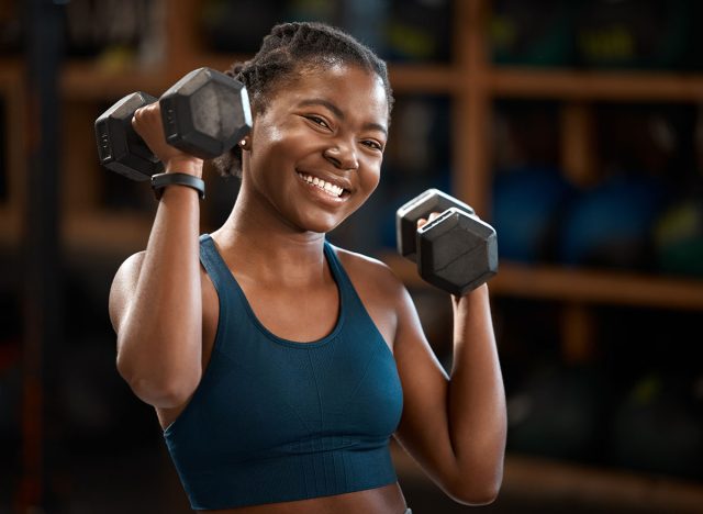 Black woman, smile and portrait with dumbbell for fitness muscle, wellness or body health challenge. Face, strong or bodybuilder weightlifting for exercise, workout or power for energy in sport club