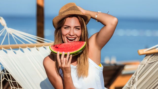 Young beautiful woman eating juicy watermelon on the beach.