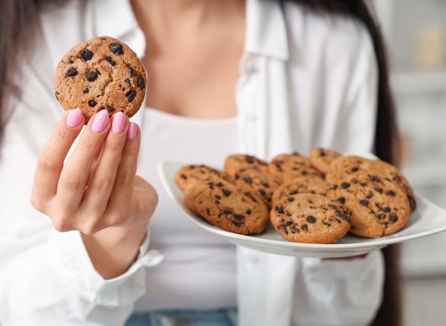 Beautiful young woman holding plate of tasty cookies with chocolate chips at home, closeup