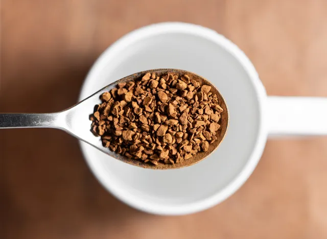 Top view of a spoon filled with instant coffee and a white cup in the background. Preparing instant coffee.