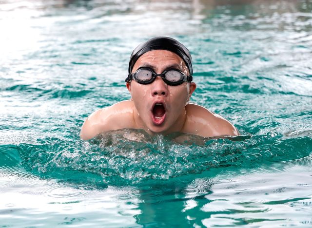 Portrait professional young Asian swimmer with cap and swim goggles open mouth and breathing during swimming butterfly in pool