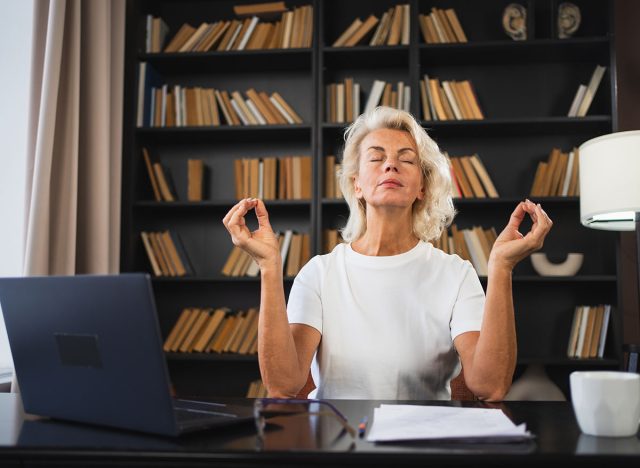 Yoga mindfulness meditation No stress keep calm. Middle aged woman practicing yoga at office. Woman taking break from work meditating relaxing. Mature lady doing breathing practice online yoga at work