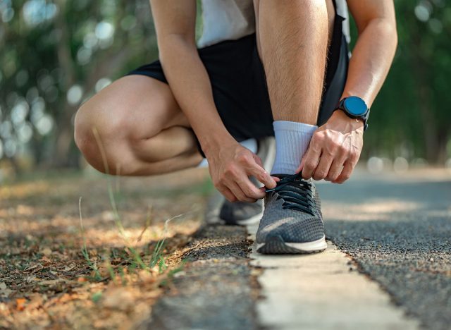 Close up - Running shoes runner man tying laces for summer run in forest park. Jogging girl exercise motivation health and fitness exercise.