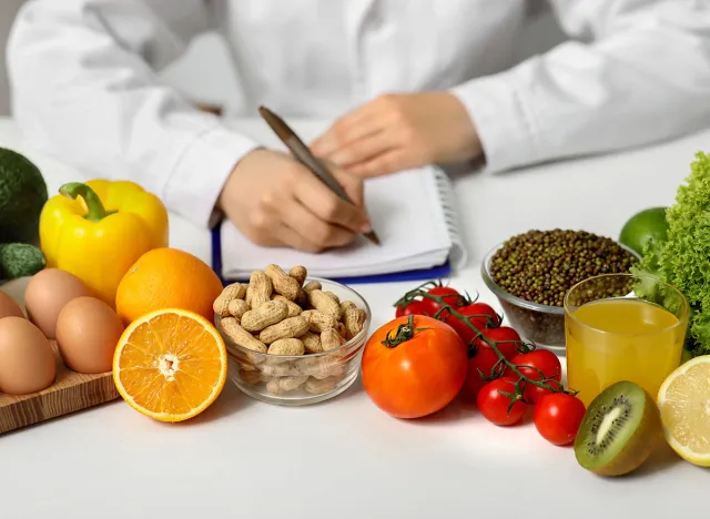 Young female nutritionist with healthy food writing diet plan in office, closeup