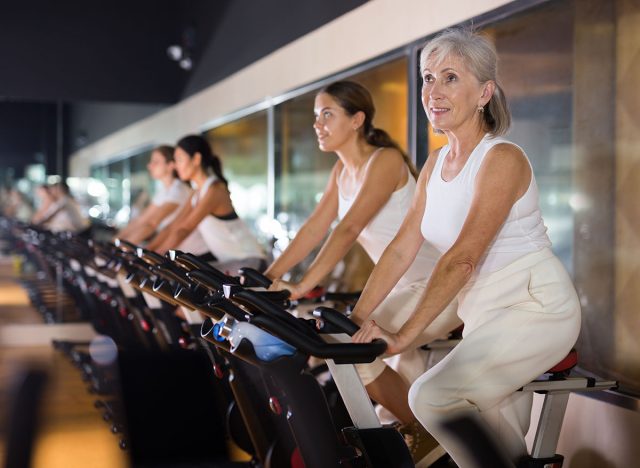 Portrait of active mature woman training on stationary bike workout in gym