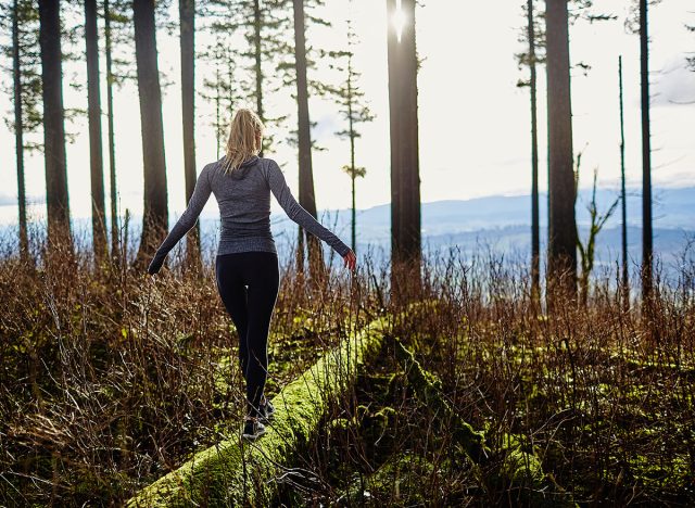 beautiful young girl walking in forest in running clothes standing on log