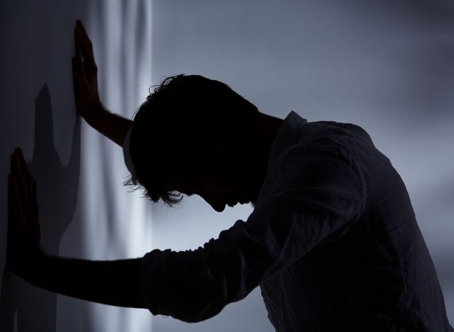 Man leaning with hands against wall, dark room