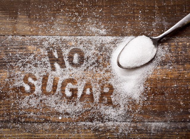 high-angle shot of a wooden table sprinkled with sugar where you can read the text no sugar and a spoon full of sugar