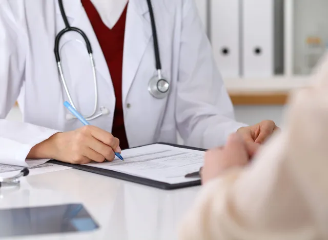 Close up of a female doctor filling up an application form while consulting patient