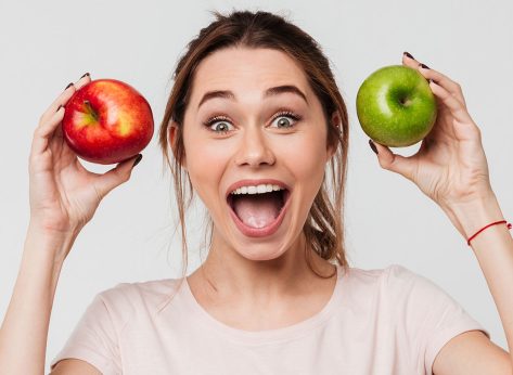 Portrait of a joyful happy girl holding apples and looking at camera isolated over white background