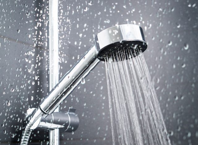 Fresh shower behind wet glass window with water drops splashing. Water running from shower head and faucet in modern bathroom.