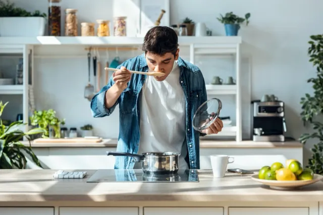 Mature man tasting the food he is preparing in the kitchen at home.