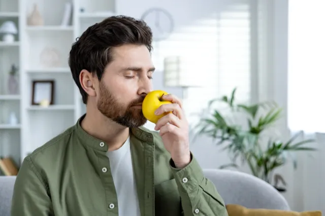 A man with a beard is peacefully smelling a fresh apple.