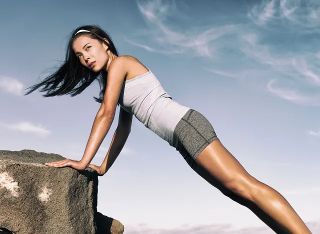 Strength training fitness woman working out core with angled push up exercise on rock. Asian athlete exercising with body weight exercises for toned body. Workout in summer desert landscape.