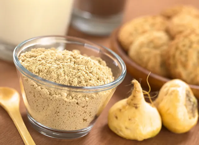 Powdered Maca or Peruvian ginseng (lat. Lepidium meyenii) in glass bowl with milk, chocolate drink, maca cookies and maca roots (Selective Focus, Focus one third into the maca powder)