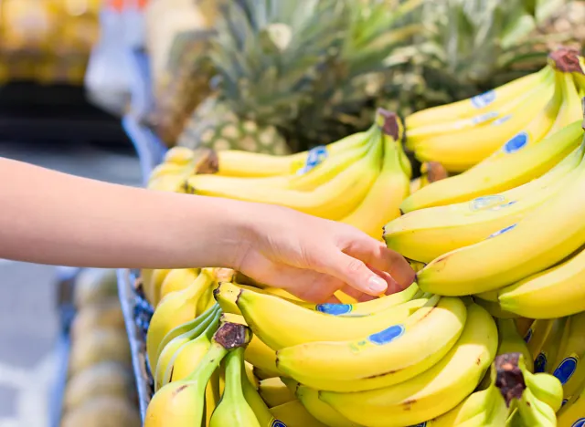 woman's hand choosing bananas from food counter in supermarket.