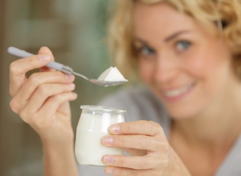 portrait of beautiful young woman eating yogurt at home