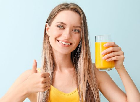 Woman with healthy juice showing thumb-up gesture on light background. Diet concept