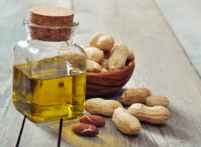 Peanut oil with raw peanuts on wooden background