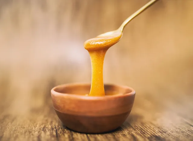 Manuka honey spoon dipped in golden liquid natural superfood on wooden background.