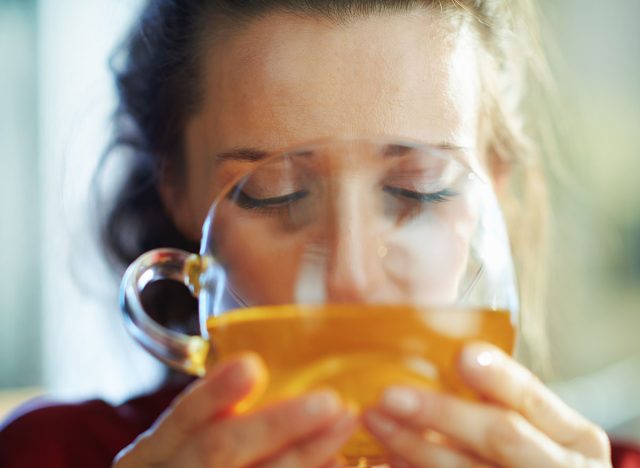 trendy 40 years old woman in black body lingerie and red bathrobe in the modern house in sunny day drinking cup of green tea.