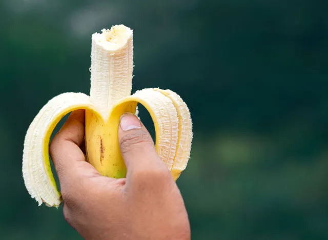 Close up of man holding peeled banana in outdoor background.