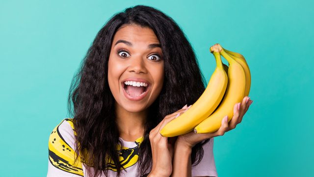 Photo of astonished dark skin girl scream hold bananas wear pink t-shirt isolated over teal color background