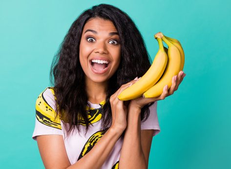 Photo of astonished dark skin girl scream hold bananas wear pink t-shirt isolated over teal color background