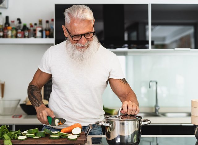 Happy senior man having fun cooking at home - Elderly person preparing health lunch in modern kitchen - Retired lifestyle time and food nutrition concept