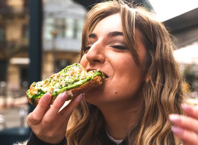 Young caucasian woman having breakfast at a terrace eating an avocado toast.