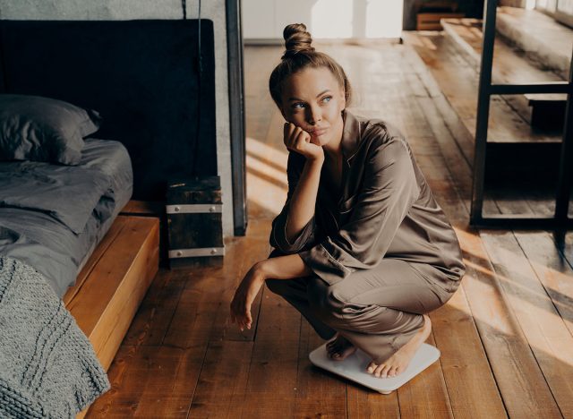 Upset and unmotivated woman on electronic floor scale in bedroom wondering why cannot lose weight despite her new diet, looking aside with sade face expression. Weight Loss and healthy lifestyle