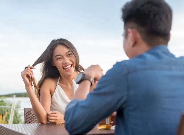 A young woman twirls her hair while listening intently to her date. Interested and attracted to a man she likes. A first date going well. Outdoor cafe scene.