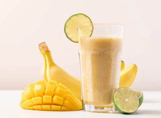 Banana mango smoothie in a tall glass on a light background. Diet breakfast. Tropical fruit drink concept