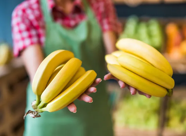 Worker in fruits and vegetables shop is holding bananas. Close up of bananas.