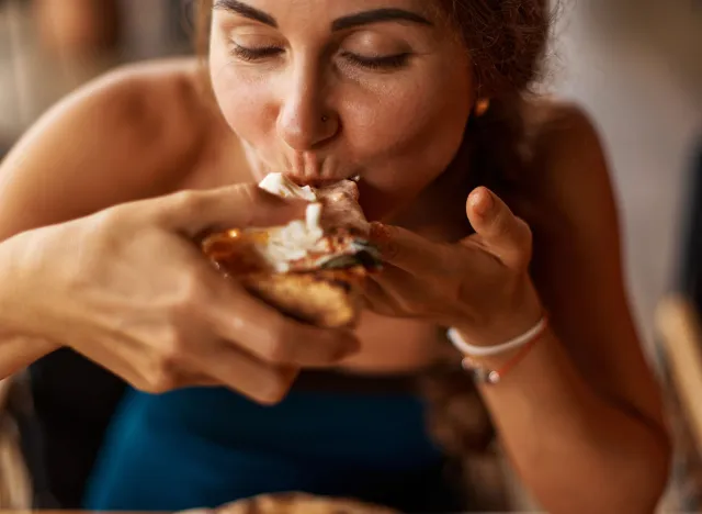 Young Caucasian suntanned beautiful elegant woman eating, biting Italian thick tomato pizza with burata cheese Yummy unhealthy food. Liking fingers