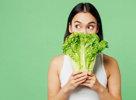 Young woman wear white clothes hold cover mouth with bunch of fresh greens lettuce leaves look aside isolated on plain pastel light green background. Proper nutrition healthy fast food choice concept