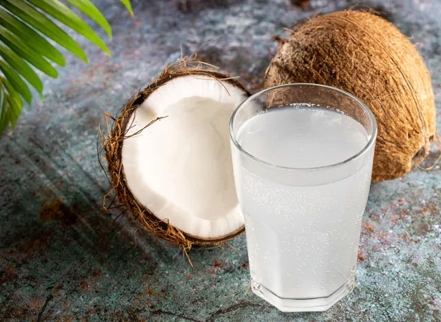 Glass with fresh coconut water and coconuts on the table.