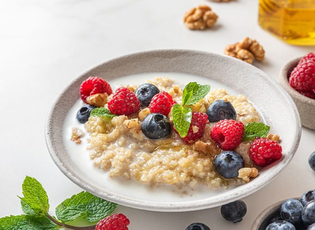 Quinoa porridge with fresh blueberry, raspberry, walnuts and mint in a bowl on white background. close up